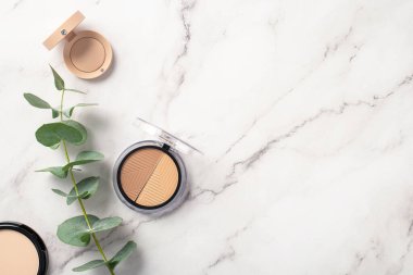 Makyaj konsepti. Beyaz mermer zemin üzerinde beyaz mermer kaplamalı göz makyajı kompakt toz ve okaliptüslerin üst görünüm fotoğrafı