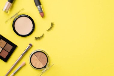 Makyaj konsepti. Makyaj fırçaları, ruj ve izole edilmiş sarı arka planda takma kirpiklerin oluşturduğu göz fotografı.