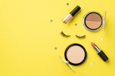 Makyaj konsepti. Üst görünüm fotoğraf palet ojeli ruj sahte kirpikler ve izole edilmiş sarı arka planda yıldız şekilli konfeti