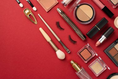 Uydurma konsept. Ruj dudak parlatıcısının üst görüntüsü. Palet göz farı, maskara sahte kirpikler, tokalar, parfüm şişesi ve kopyalanmış kırmızı arka plan.