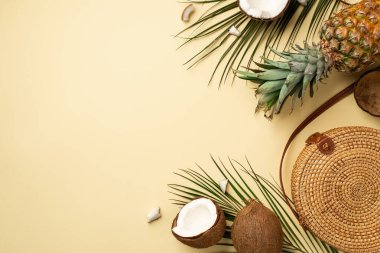Yaz tatili konsepti. Yuvarlak rattan el çantasının üst görüntüsü taze tropikal meyveler çatlak hindistan cevizi ananas ve yeşil palmiye yaprakları izole edilmiş bej arka planda boş alan