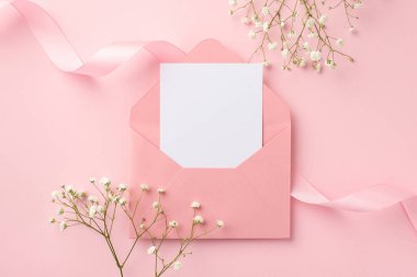 Düğün davetiyesi konsepti. Açık pembe zarf, kağıt kart, kıvrımlı kurdele ve beyaz çigila çiçeklerinin izole edilmiş pastel pembe arka plan ve boş alan.