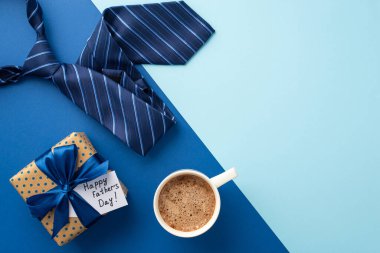 Babalar Günü konsepti. Kırmızı noktalı hediye kutusunun üst görüntüsü. Kurdele yayı, kahve fincanı ve mavi kravat, iki renkli mavi arka plan, boş alan.