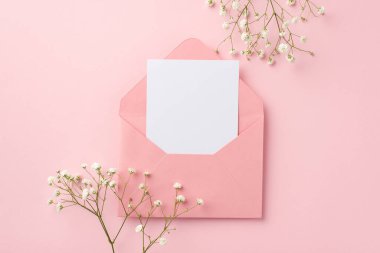 Düğün davetiyesi konsepti. Kartvizitli açık pembe zarf ve izole edilmiş pastel pembe arka planda beyaz çigila çiçekleri.