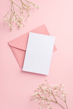 Parti davetiyesi konsepti. Pembe zarf kâğıdının dikey üst görüntüsü ve izole edilmiş pastel pembe arkaplandaki beyaz çigila çiçekleri boş alan