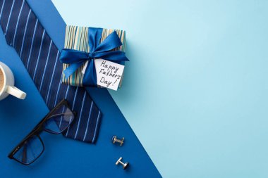 Babalar Günü konsepti. İpek kurdeleli son moda hediye kutusunun üst görünümü ve boş arkaplan ile bicolor mavi arka plan üzerinde sıcak içme gözlüğü ve mavi kravat fincanı.