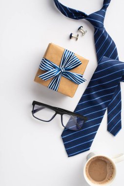 Babalar Günü konsepti. El işi kağıt hediye kutusunun dikey üst görüntüsü. Kurdele, papyon, mavi kravat, kahve bardağı ve izole edilmiş beyaz arka planda kol düğmeleri.