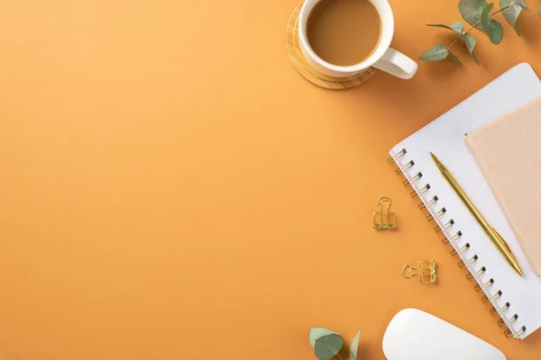 Business concept. Top view photo of workplace cup of coffee on wooden stand white computer mouse notepads gold pen binder clips and eucalyptus sprig on isolated orange background with empty space