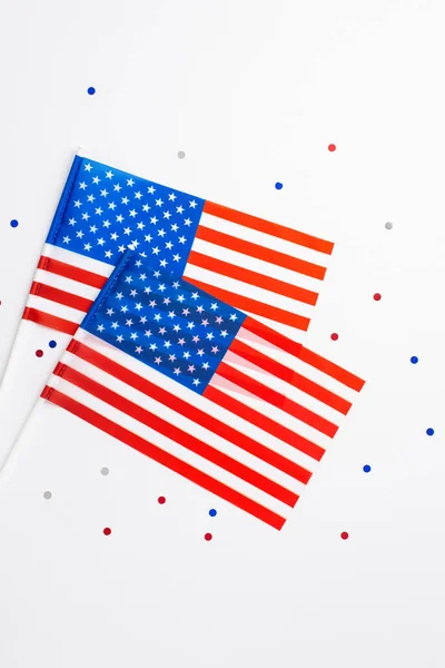 USA Independence Day concept. Top view vertical photo of two national flags and confetti on isolated white background