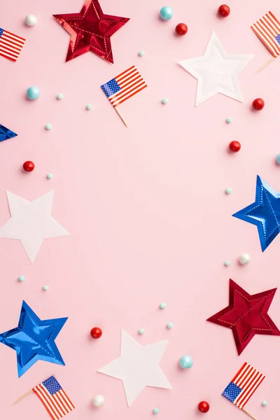 Fourth of July concept. Top view vertical photo of US national flags stars and scattered candies on isolated pastel pink background with empty space in the middle