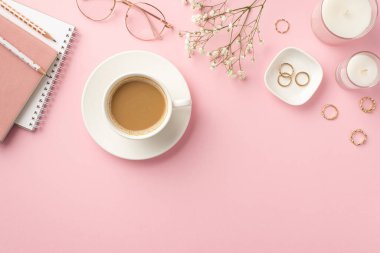İş konsepti. İş yeri mumlarının en üstteki fotoğrafı günlükler fincan fincan kahve kalemleri şık bardaklar altın yüzükler ve izole edilmiş pastel arka planda beyaz çingene çiçekleri.