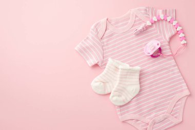 Bebek aksesuarları konsepti. Pembe bebek kıyafetlerinin üst görüntüsü vücut giysisi çorapları ve izole edilmiş pastel arka planda emzik zinciri.