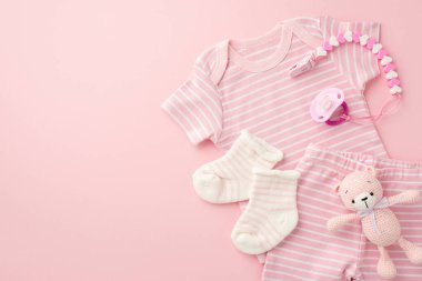 Bebek aksesuarları konsepti. Pembe bebek kıyafetlerinin, şortunun, oyuncak ayının çorabının ve emzik zincirinin izole edilmiş pastel arka planda üst görüntüsü.
