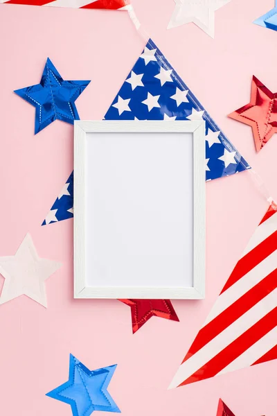 USA Independence Day concept. Top view vertical photo of photo frame over national flag garland and stars on isolated pastel pink background with empty space