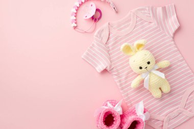 Bebek aksesuarları konsepti. Pembe bebek kıyafetlerinin üst görüntüsü vücut giysisi patik emzik zinciri ve izole edilmiş pastel pembe arka planda örülmüş tavşan oyuncağı boş alan