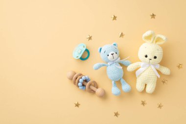 Bebek aksesuarları konsepti. Örgü örülmüş tavşan ve oyuncak ayıların en üstteki fotoğrafı ahşap çıngırak mavi emzik ve izole edilmiş pastel bej arka planda altın yıldızlar