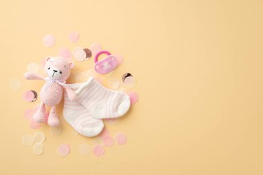 Bebek aksesuarları konsepti. Pembe örülmüş oyuncak ayının en iyi fotoğrafı rahatlatıcı çoraplar ve izole edilmiş pastel bej arka planda parlak konfeti.