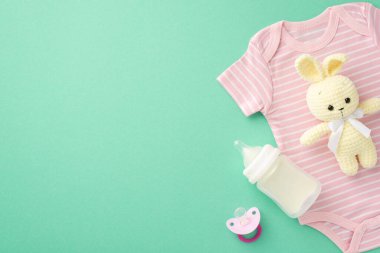 Bebek aksesuarları konsepti. Bebek kıyafetlerinin üst görüntüsü pembe tulum örülmüş oyuncak süt şişesi ve izole edilmiş deniz mavisi arka planda emzik.