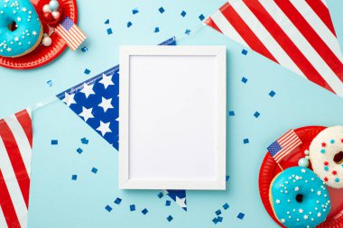 4 Temmuz konsepti. Fotoğraf çerçevesinin en üst görüntüsü ulusal bayrak konfeti levhaları izole edilmiş pastel mavi arka planda boş alan ile donut ve şekerler