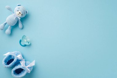 Bebek aksesuarları konsepti. Örgü örülmüş oyuncak ayının en üstteki fotoğrafı küçük patik ve emzik izole edilmiş pastel mavi arka planda kopyalanmış