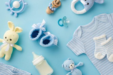 Bebek aksesuarları konsepti. Bebek kıyafetlerinin üst görüntüsü mavi gömlek örülmüş patik çoraplar tavşan ve oyuncak ayılar süt şişesi ve emzik izole edilmiş pastel mavi arka planda.