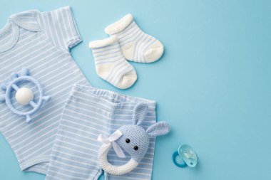 Bebek aksesuarları konsepti. Mavi bebek kıyafetlerinin, iç çamaşırlarının, çorapların, oyuncak bağcıklarının ve emziğin izole edilmiş pastel mavi arka planda üst görüntüsü.