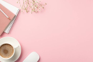 İş konsepti. Çalışma alanının en üst görüntüsü notlar kalem fincan fincan fincan fincan fincan fincan bilgisayar fare ve izole edilmiş pastel pembe arka plan üzerinde beyaz çigila çiçekler boş alan