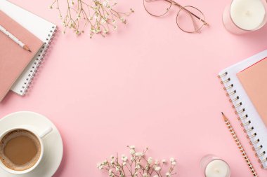 İş konsepti. Çalışma alanının en üst görüntüsü notlar kahve fincanları çay tabağı mumları bardaklar ve beyaz çigila çiçekleri izole edilmiş pastel pembe arka plan ve ortada boş alan.