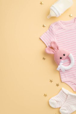 Bebek aksesuarları konsepti. Bebek kıyafetlerinin dikey fotoğrafı. Pembe beden giysisi, küçük çorap şişesi, çıngıraklı tavşan çıngıraklı oyuncak ve izole edilmiş pastel bej arka planda altın yıldızlar.