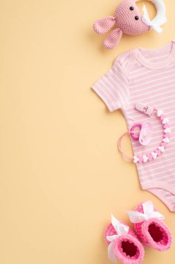 Bebek aksesuarları konsepti. Bebek kıyafetlerinin dikey fotoğrafı pembe tulumlar örgü ayakkabılar, çıngırak oyuncaklar ve izole edilmiş pastel bej arka planda emzik zinciri.