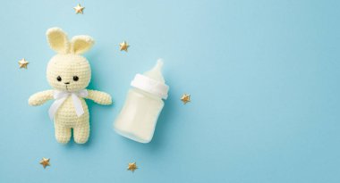 Bebek aksesuarları konsepti. Örgü örülmüş tavşan oyuncak süt şişesi ve altın yıldızların, izole edilmiş pastel mavi arka planda fotosu.