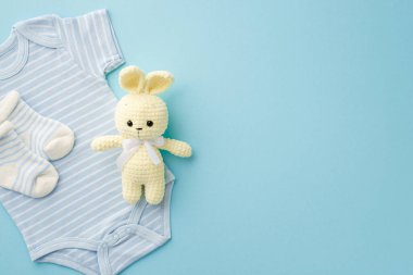 Bebek aksesuarları konsepti. Bebek kıyafetleri, mavi vücut giysisi çorapları ve pastel mavi arka planda örülmüş tavşan oyuncağı.