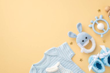Bebek oğlan konsepti. Mavi bebek kıyafetlerinin üst görüntüsü vücut giysisi çoraplar örülmüş tavşan çıngıraklı oyuncak bağlayıcısı ve izole edilmiş pastel bej arka planda altın yıldızlar.