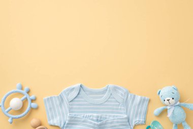 Bebek oğlan konsepti. Üst görüntüde mavi bebek kıyafetleri gömleği iç çamaşırları çıngırak emziği ve izole edilmiş pastel bej arka planda örülmüş oyuncak oyuncak.