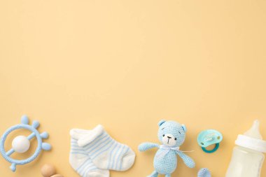 Bebek oğlan konsepti. Örülmüş oyuncak ayının üst görüntüsü mavi çıngıraklı süt şişesi emziği ve izole edilmiş pastel bej arka planda küçük çoraplar.