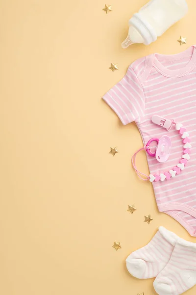 婴儿用品概念 婴儿衣服粉色紧身衣小袜子奶瓶奶嘴链子和孤立的淡黄色背景上的金色星星的倒立照片 — 图库照片