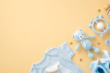 Bebek oğlan konsepti. Mavi bebek kıyafetlerinin üst görüntüsü vücut giysisi çoraplar oyuncak ayı bağcığı örgü ve izole edilmiş pastel bej arka planda altın yıldızlar boş alan