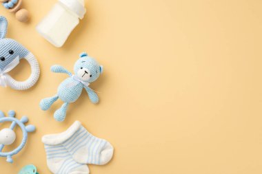 Bebek aksesuarları konsepti. Örgü örülmüş tavşan çıngıraklı oyuncak oyuncak oyuncak oyuncak oyuncak mavi ip süt şişesi ve izole edilmiş pastel bej arka planda küçük çoraplar.