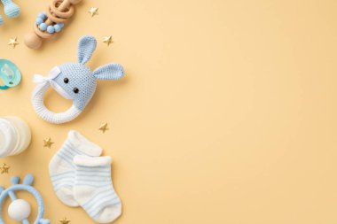 Bebek aksesuarları konsepti. Örgü örülmüş tavşan çıngıraklı tavşan, oyuncak, mavi zincir, tahta, çıngıraklı süt şişesi, yumuşatıcı ve altın yıldızların izole edilmiş pastel bej arka planda çekilmiş fotoğrafı.