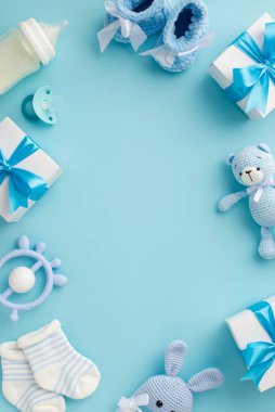 Bebek konsepti. Hediye kutularının dikey fotoğrafı çoraplar, emzik oyuncak bebek sütü şişesi ve izole edilmiş pastel mavi arka planda örülmüş tavşan çıngırağı oyuncağı ortada da kopyalanmış boşluk.