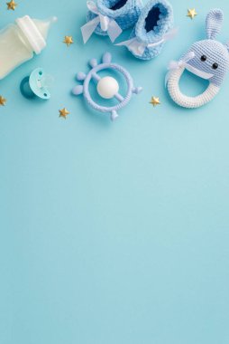 Bebek oğlan konsepti. Ganimet emziğinin dikey resmi süt şişesi, örülmüş tavşan çıngıraklı oyuncak ve altın yıldızlar, izole edilmiş pastel mavi arka planda, kopyalanmış mavi arka planda.