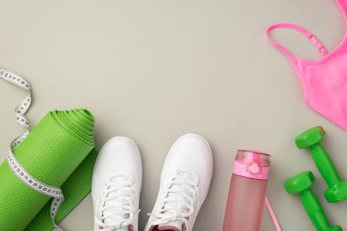 Spor aksesuarları konsepti. Beyaz ayakkabıların en üstteki fotoğrafı pembe spor sutyen şişesi su bandı ölçümü yeşil egzersiz paspası ve izole edilmiş pastel gri arka plan üzerindeki dambıllar