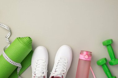 Fitness konsepti. Beyaz spor ayakkabılarının üst görüntüsü pembe su bandı şişesi yeşil egzersiz minderi ve izole edilmiş pastel gri arka plandaki halterleri ölçer boş alan