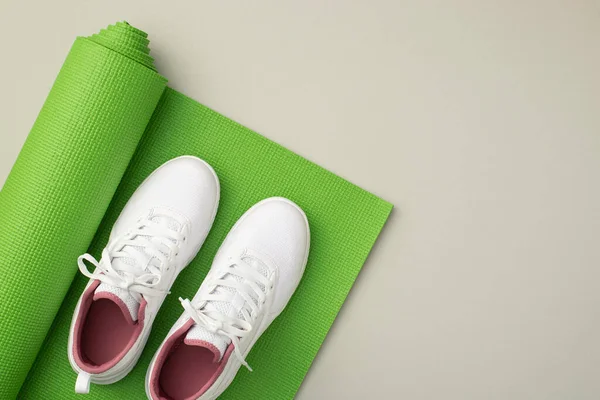 Sports accessories concept. Top view photo of white sneakers over green yoga mat on isolated pastel grey background