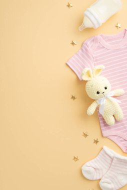 Bebek aksesuarları konsepti. Bebek kıyafetlerinin dikey fotoğrafı pembe vücut giysisi çoraplar, örgü tavşan oyuncakları ve izole edilmiş pastel bej arka planda altın yıldızlar.