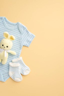 Bebek aksesuarları konsepti. Mavi bebek kıyafetleri, vücut giysisi çorapları ve izole edilmiş pastel bej arka planda örülmüş tavşan oyuncağı.
