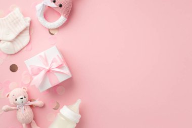 Bebek aksesuarları konsepti. Örgü örülmüş tavşan çıngıraklı yılan oyuncağı hediye kutusu oyuncak ayıcıklı oyuncak süt şişesi ve izole edilmiş pastel pembe arka planda parlak konfeti.