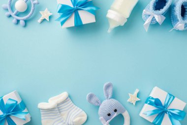 Bebek aksesuarları konsepti. Hediye kutularının en üstteki fotoğrafı örgü örülmüş tavşan çıngıraklı oyuncak çoraplar süt şişesi ve yıldızlar izole edilmiş pastel mavi arka planda boş alan