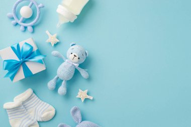 Bebek aksesuarları konsepti. Hediye kutusunun en üstteki fotoğrafı bağcıklı tavşan çıngıraklı oyuncak çoraplar süt şişesi ve yıldızlar izole edilmiş pastel mavi arka planda boş alan