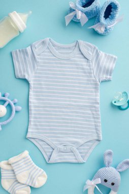 Bebek aksesuarları konsepti. Bebek kıyafetlerinin dikey fotoğrafı bebek kıyafetleri çorapları, bebek sütü şişesi ve izole edilmiş pastel mavi arka planda örülmüş tavşan çıngırağı oyuncağı.